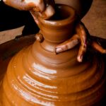 Artisan shaping a clay pot on a pottery wheel, showcasing craftsmanship and skillful technique.